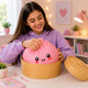 Girl playing with a pink plush toy in a yellow container at a table.