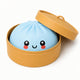 Cute plush toy resembling a steamed bun with a smiling face in a yellow container on a white background