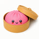 Pink dumpling plush toy with a smiling face in a tan container on a white background