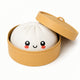 Stuffed toy resembling a dumpling with a smiling face in a yellow container on a white background